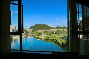 A view through a window of a building overlooking a river, with greenery and distant hills. - Longhuyuan Hostel (Yanshan)