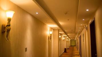 A hotel hallway with wall sconces, carpeted flooring, and doors on both sides.