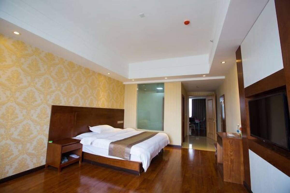 Una habitación de hotel con una cama grande, cabecera de madera, televisión y escritorio.
