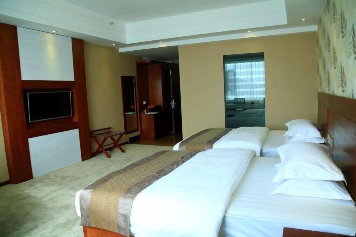 Habitación de hotel con dos camas, televisión, escritorio y puerta que da a un balcón.
