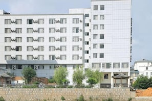A multi-story building with a grid-like facade, air conditioning units, and a traditional-style structure in the foreground.