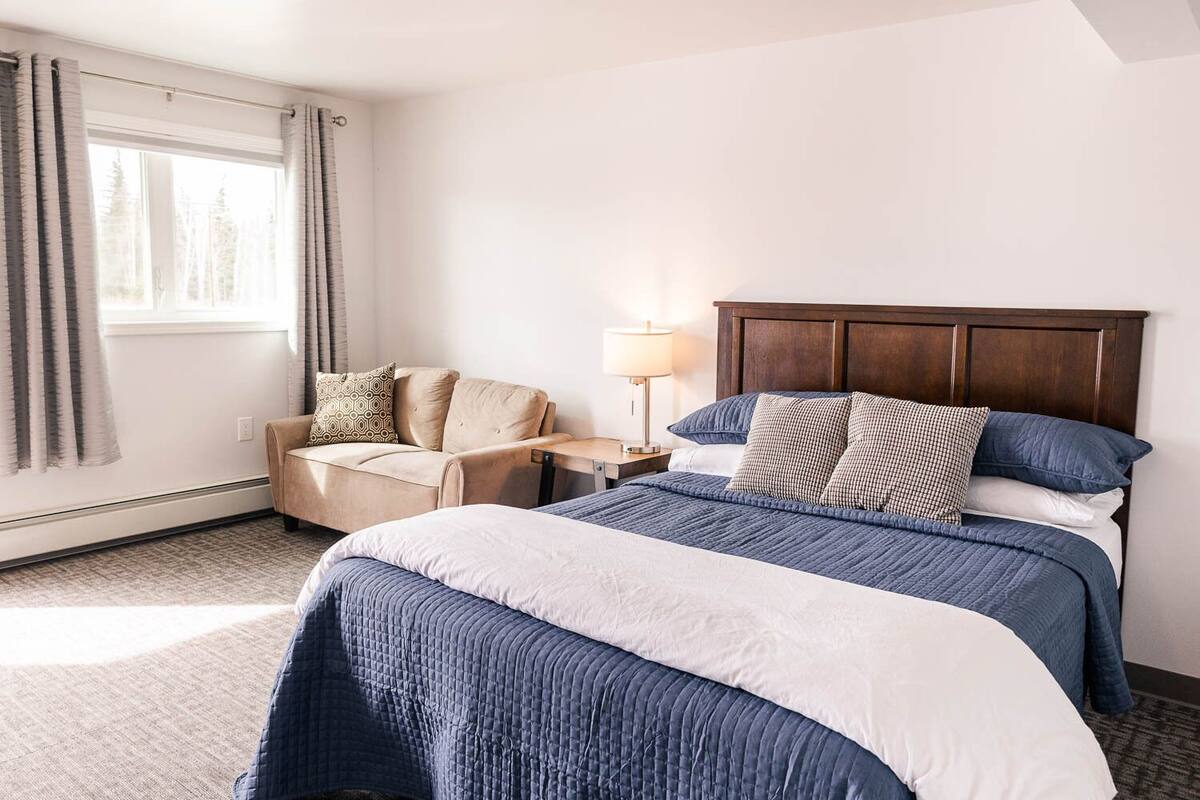 A hotel room with a large bed, a sofa, a nightstand, and a window with curtains.