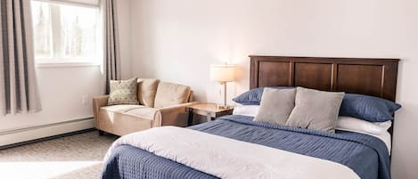 Una habitación de hotel con una cama grande, un sofá, una mesita de noche y una ventana con cortinas.