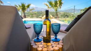 En flaska vin och två glas på ett träbord med utsikt över en pool och palmer.