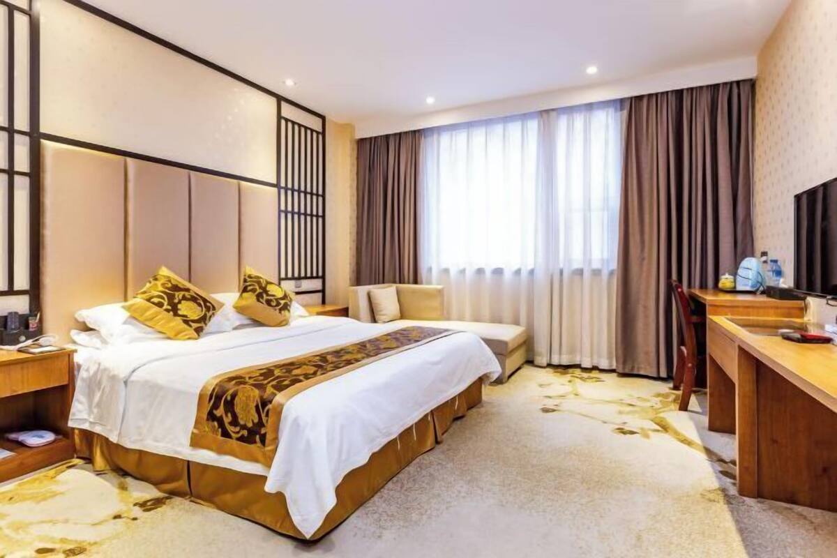 A hotel room with a large bed, a desk, a chair, a TV, and a window with curtains.