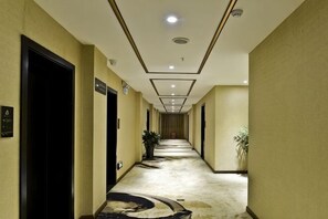 Un pasillo de hotel con piso alfombrado, puertas a ambos lados y una planta a la derecha.
