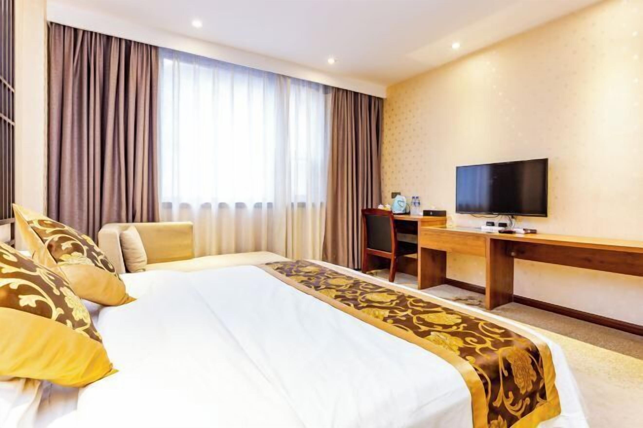 A hotel room with a bed, a desk, a television, and a window with curtains.
