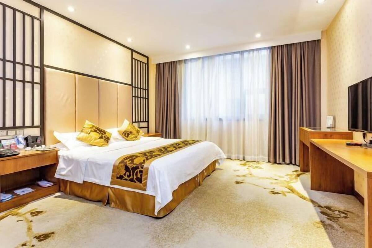 A hotel room with a bed, a desk, a television, and a large window with curtains.