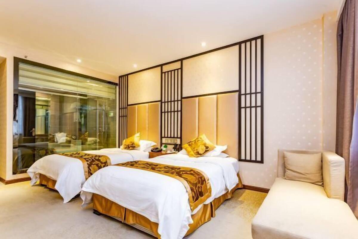 A hotel room with two beds, a sofa, and a glass partition.