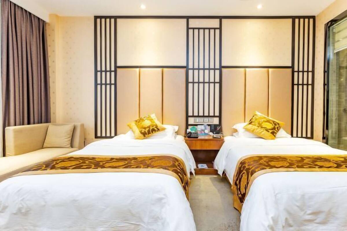 A hotel room with two beds, a sofa, a desk, and a large window.