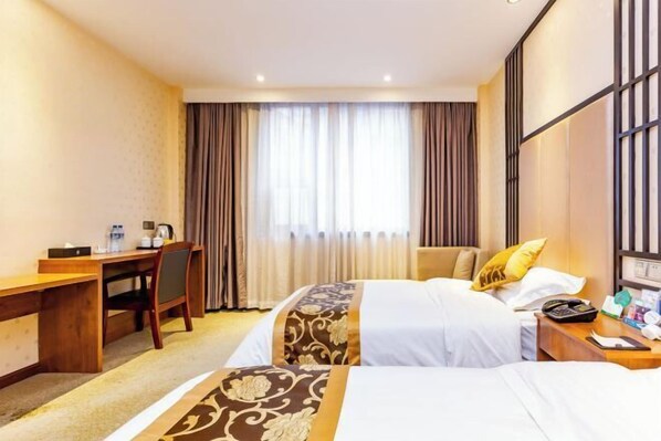 Habitación de hotel con escritorio, dos camas, una silla, ventana con cortinas y mesita de noche con teléfono y lámpara.