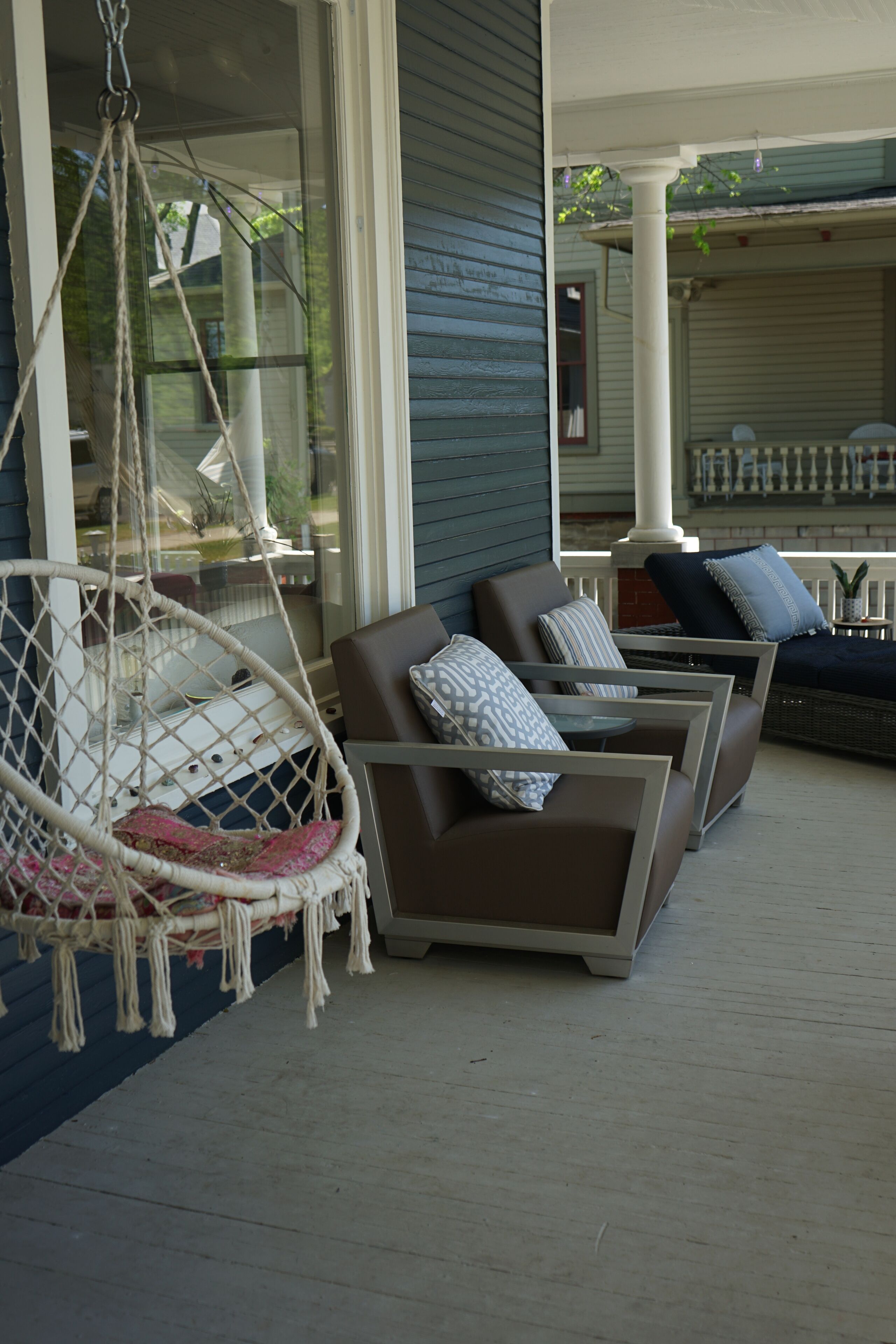 Un porxo amb una cadira penjant, dos sofàs marrons amb coixins estampats i una taula petita.