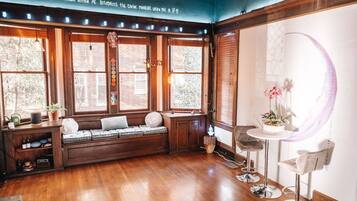 Una habitación acogedora con un banco empotrado, una pequeña mesa con sillas y ventanas grandes con cortinas.