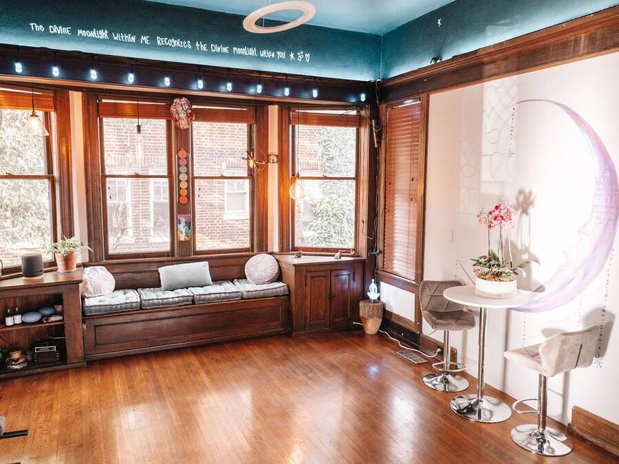 A cozy room with a built-in bench, a small table with chairs, and large windows with curtains.