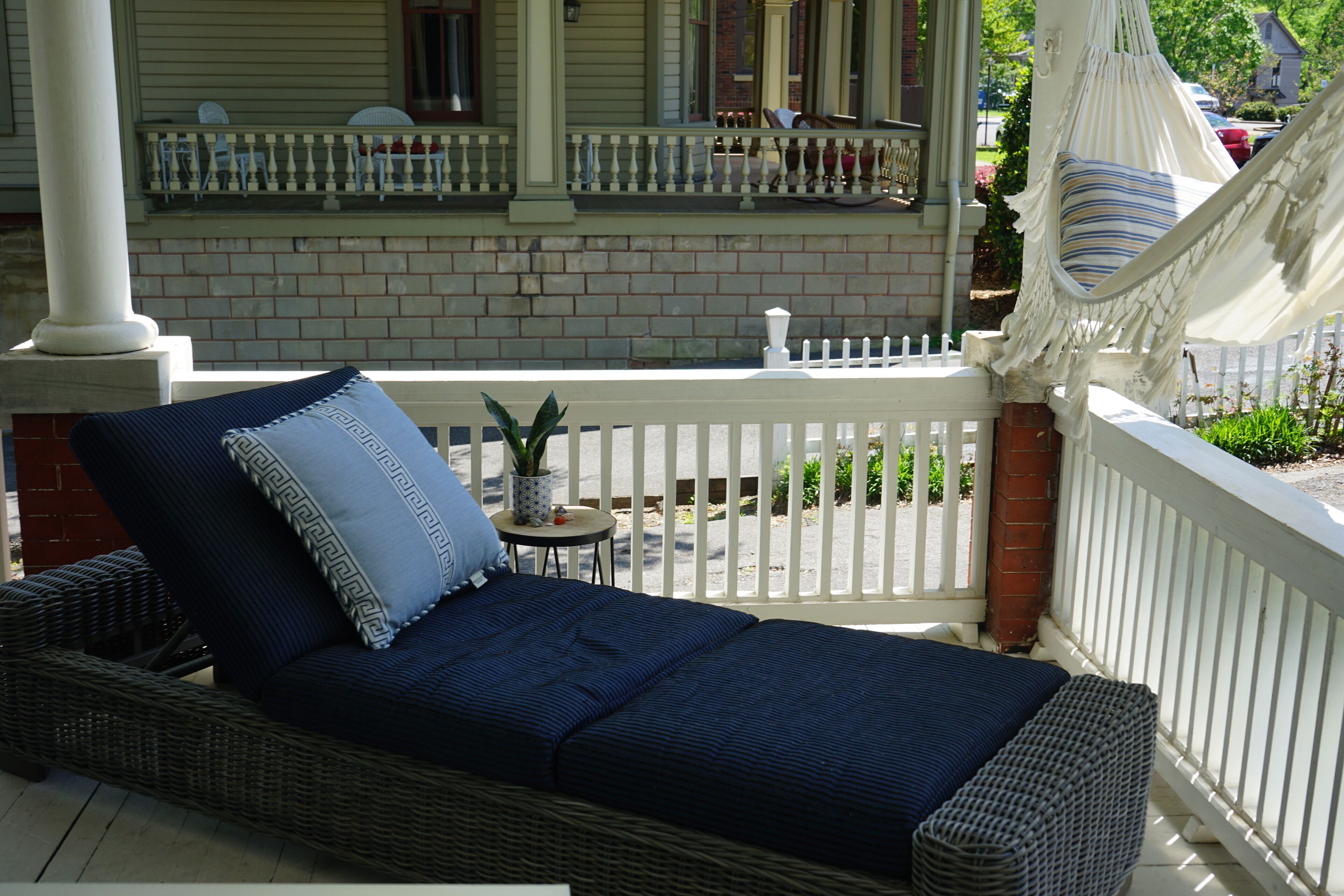 A wicker sofa with a blue cushion and a small table with a potted plant on a porch with a white fence.
