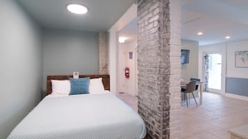 Un dormitorio con cama, pared de ladrillo decorativa, escritorio con silla y puerta que da a otra habitación.