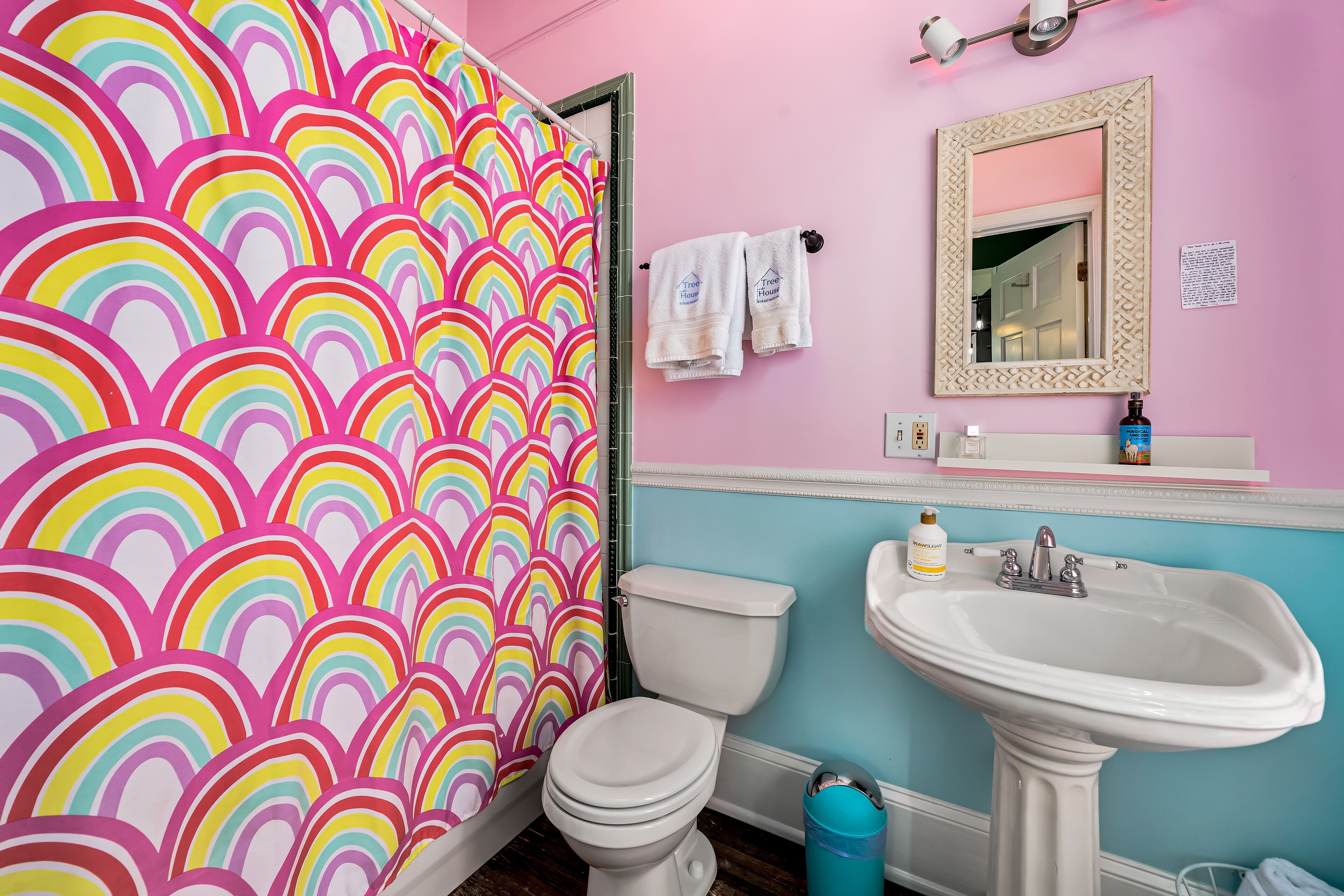 A bathroom with a colorful rainbow shower curtain, a white toilet, a sink, and a mirror.
