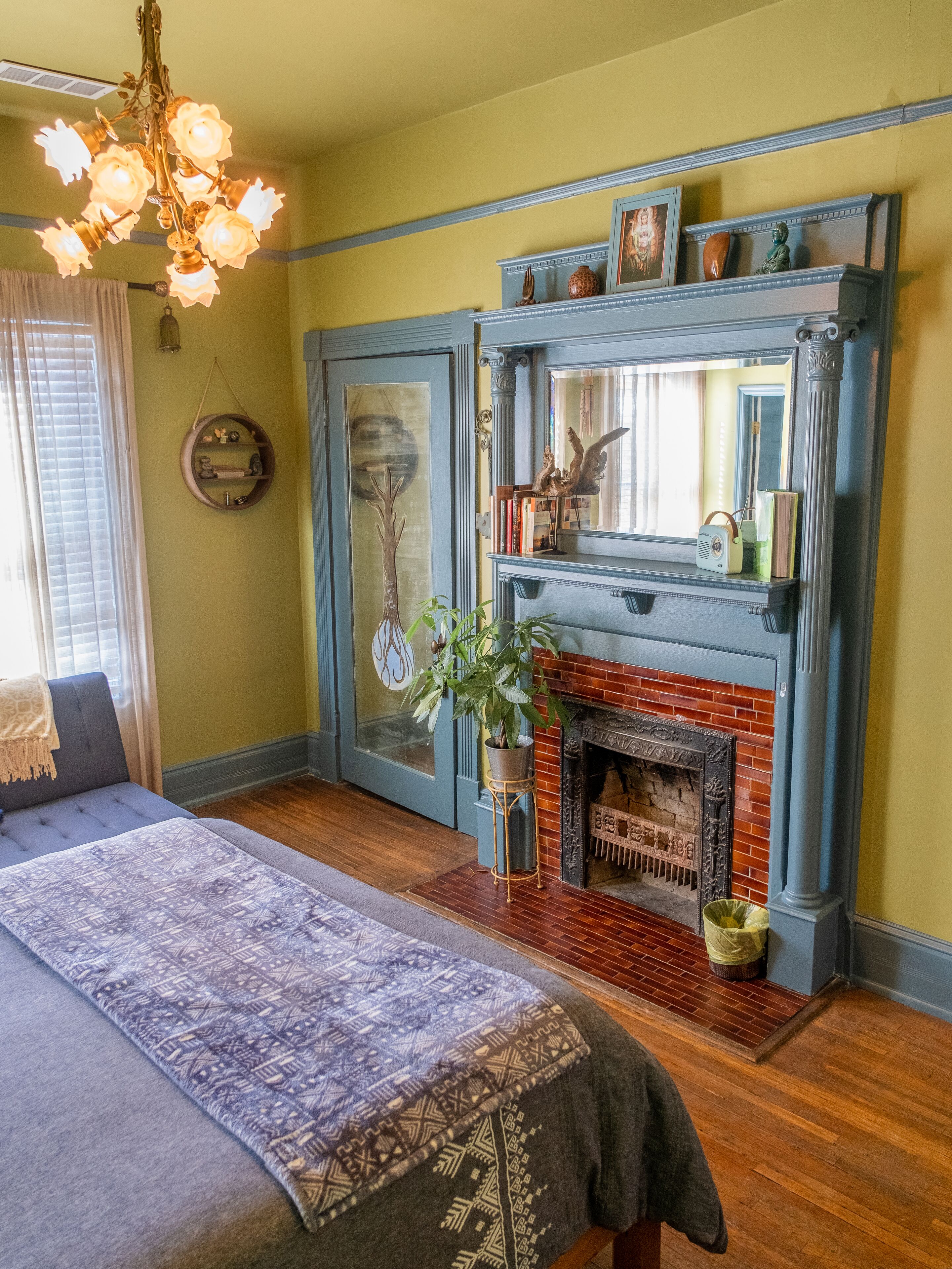 A bedroom with a bed, a fireplace, a chandelier, and a window with blinds.