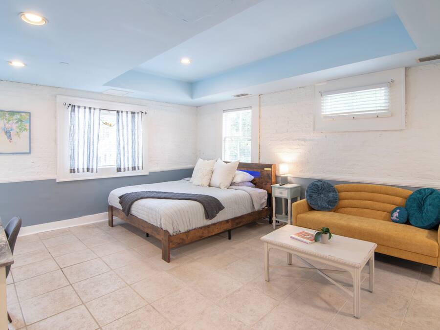 A bedroom with a bed, a sofa, a small table, and a window.