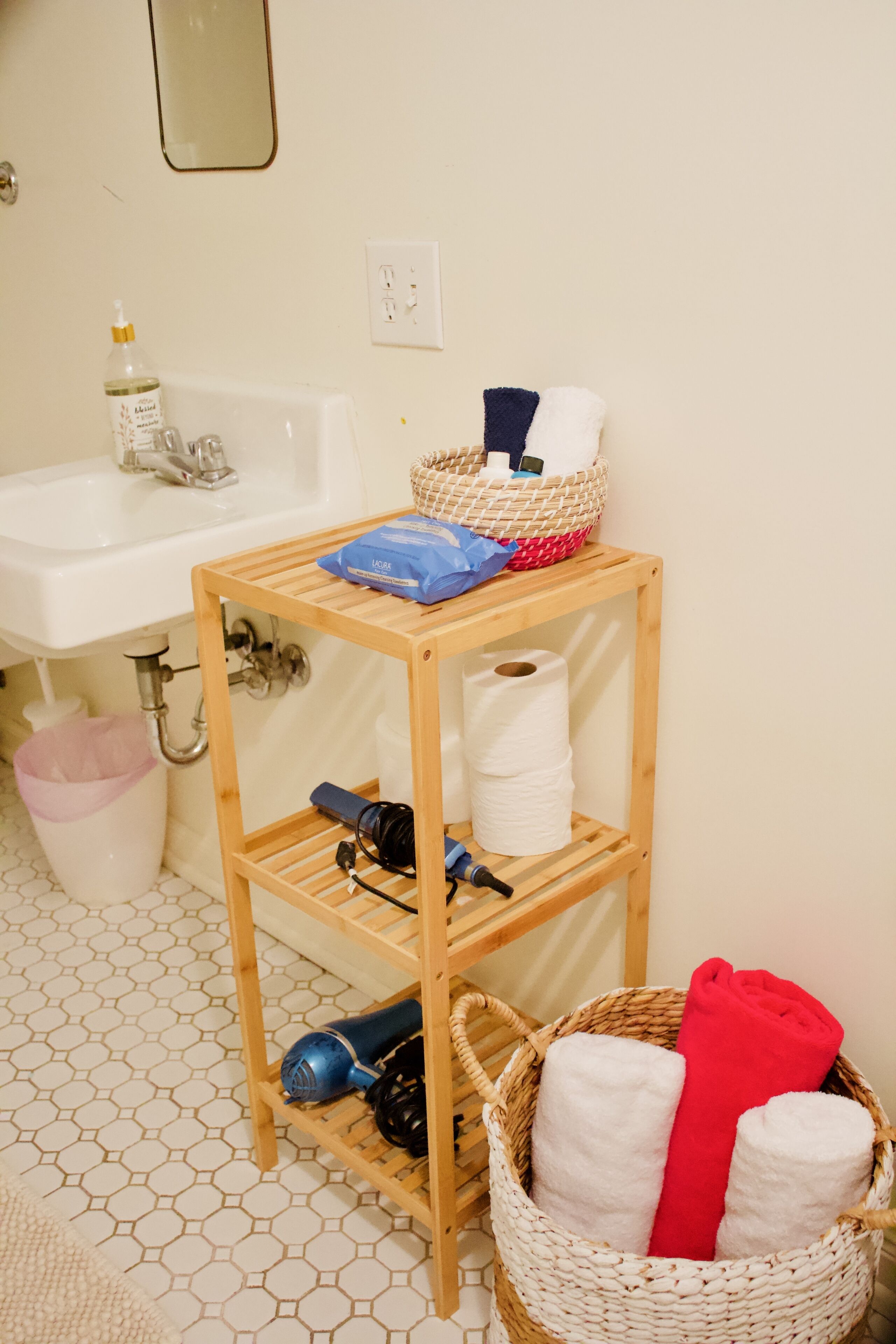 Un baño con estante de madera que contiene artículos de aseo y una cesta con toallas.