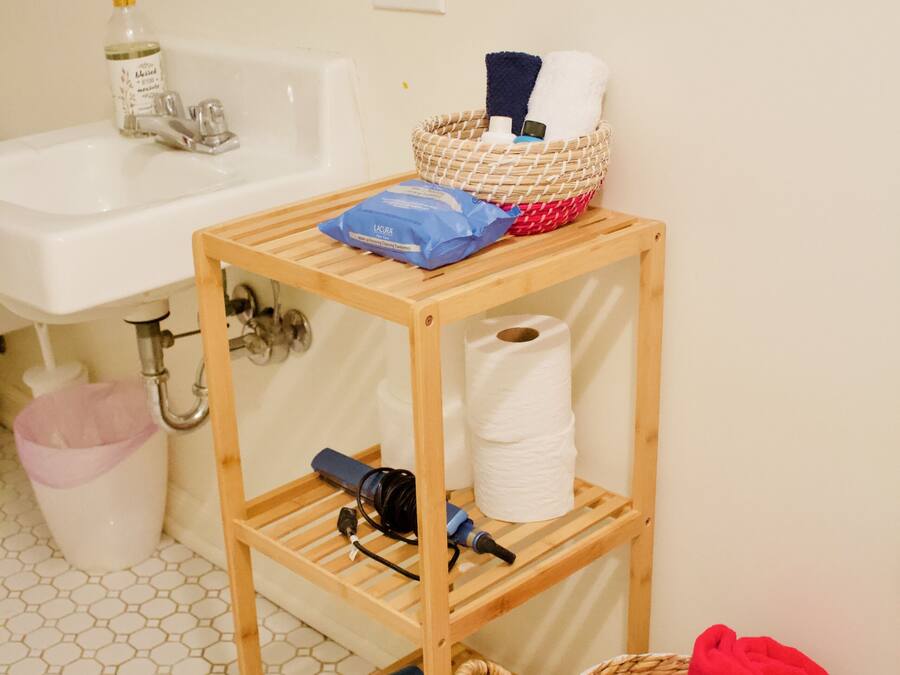 Un baño con estante de madera que contiene artículos de aseo y una cesta con toallas.