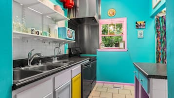A kitchen with teal walls, a pink window, and a variety of appliances and utensils.