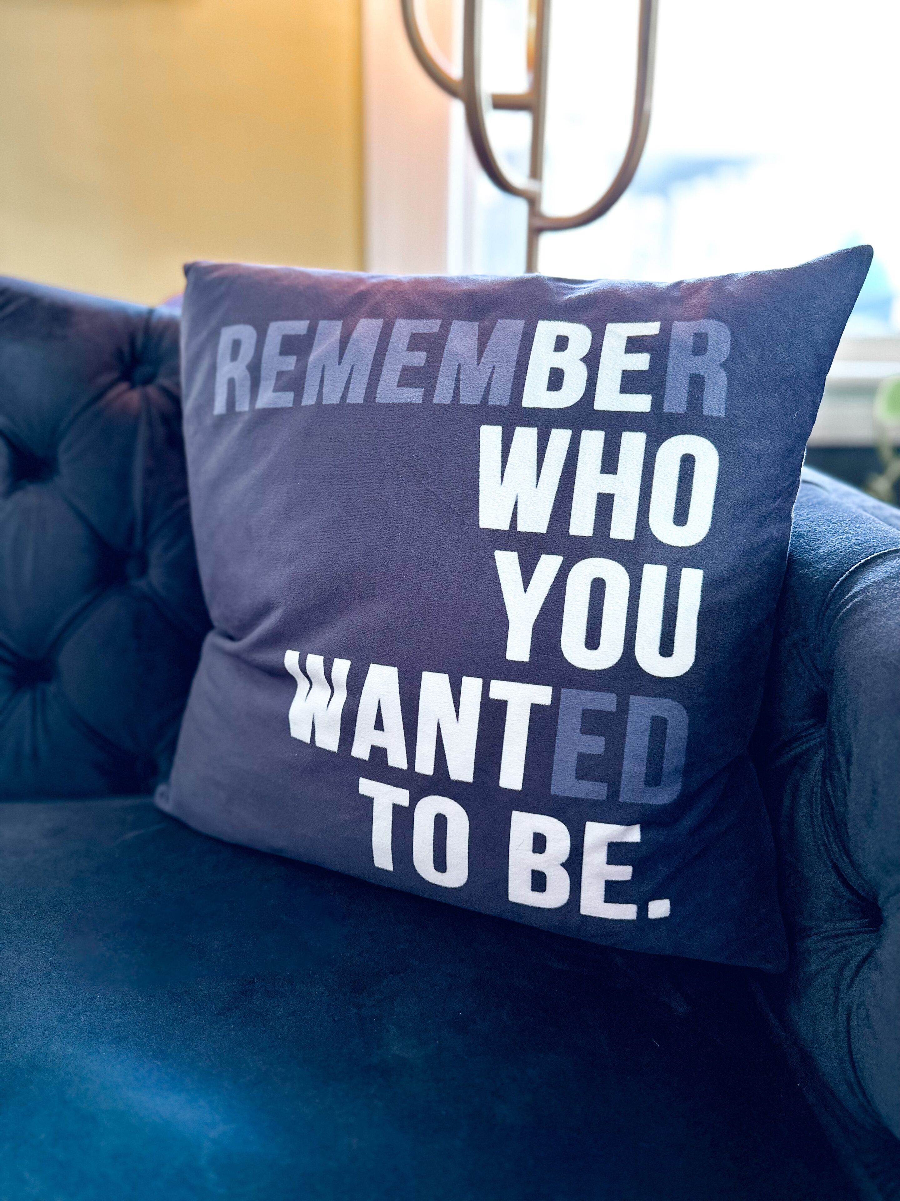 Un sofá azul oscuro con un cojín que tiene texto blanco que dice "REMEMBER WHO YOU WANTED TO BE".
