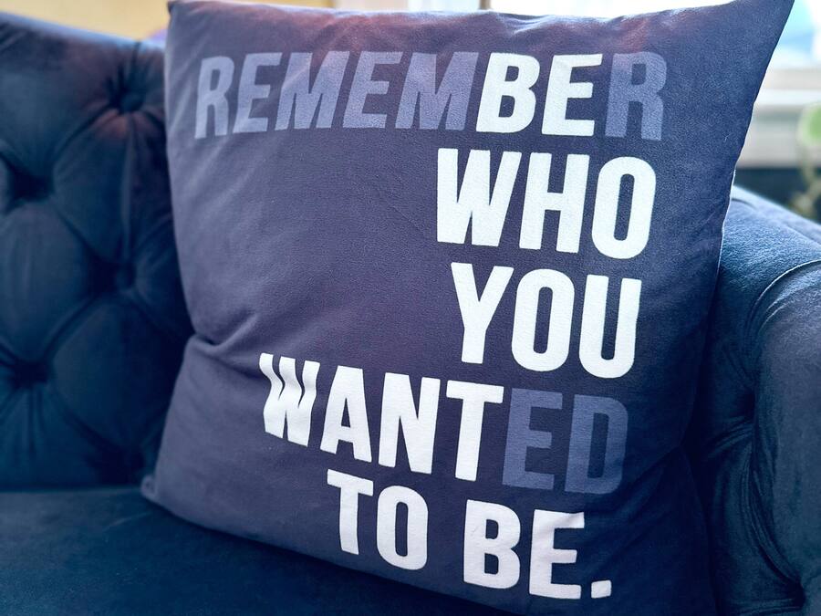 Un sofá azul oscuro con un cojín que tiene texto blanco que dice "REMEMBER WHO YOU WANTED TO BE".
