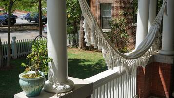 A porch with a white railing, a hammock, and a potted plant.