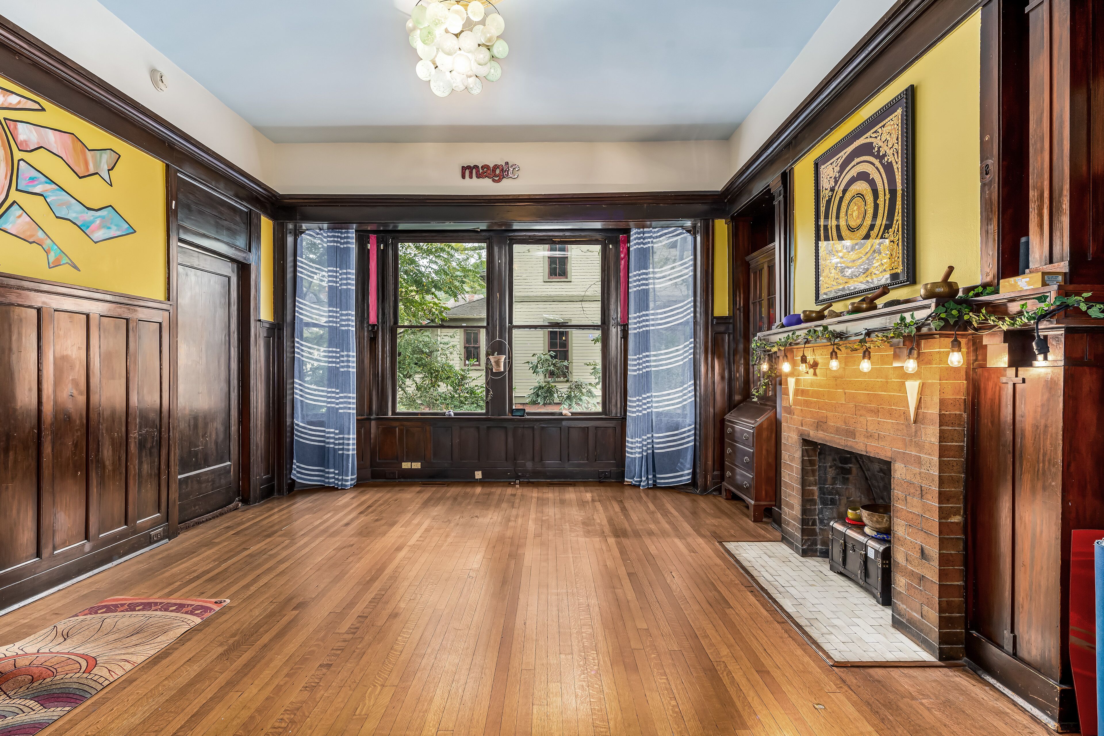 A spacious room with wooden floors, a fireplace, and large windows with curtains.