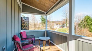 A covered porch with wicker furniture and a small table, overlooking a residential area.