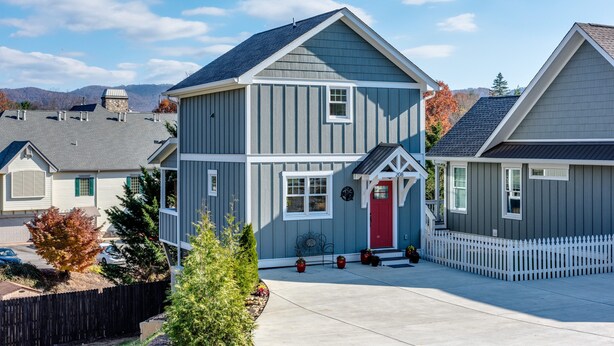 A two-story house with a red front door, a white picket fence, and a driveway leading to the entrance.