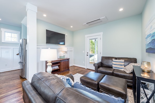 A modern living room with a brown leather sofa, a flat-screen TV mounted on the wall, and a wooden cabinet with a lamp. - Guesthouse, downtown Weaverville 2 blocks from Main St. (Weaverville)