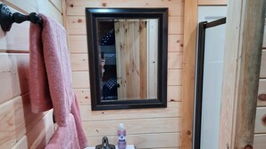 Ein kleines Badezimmer in einer Holzhütte mit Waschbecken, Spiegel und Handtuchhalter.