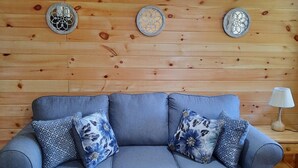 Un canapé gris agrémenté de coussins à motifs floraux, un tapis rayé aux couleurs vives et des assiettes décoratives accrochées à un mur en bois.
