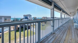 Um deck de madeira coberto com guarda-corpos brancos, com vista para uma praia e casas.