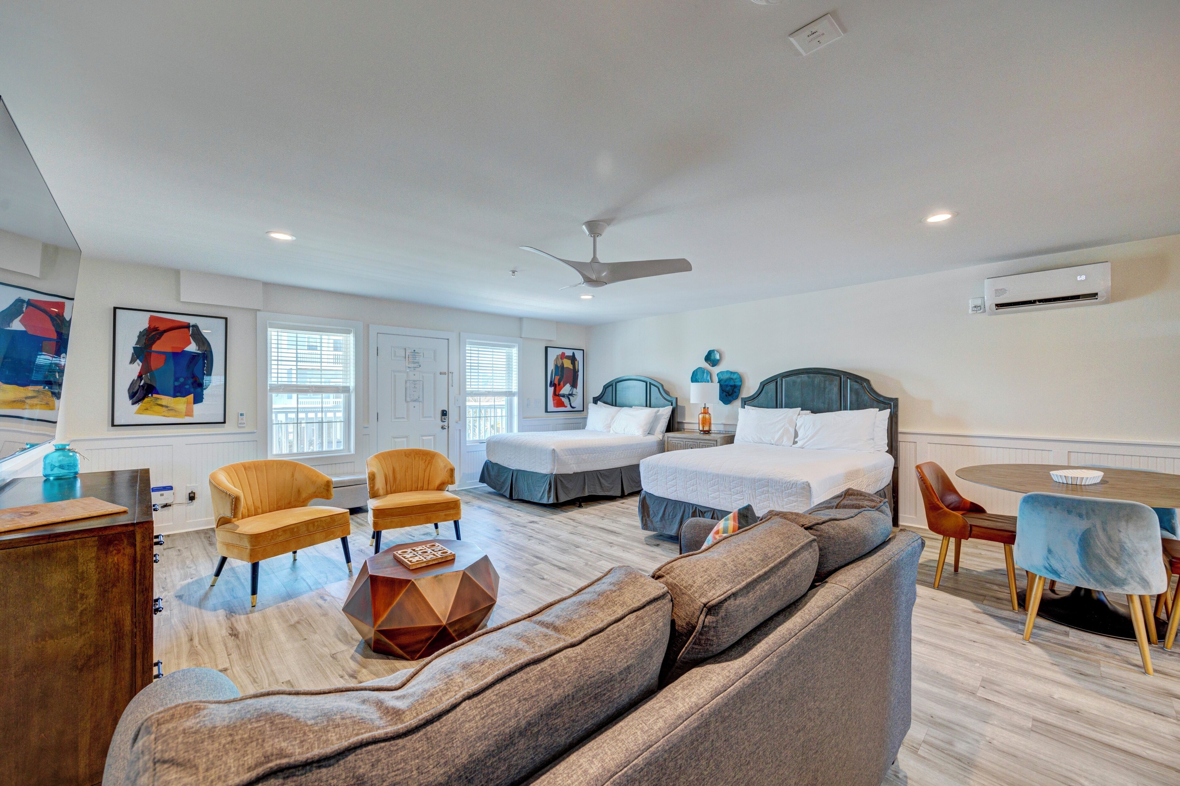 A modern hotel room with a large bed, two chairs, a sofa, a dining table, and artwork on the walls.