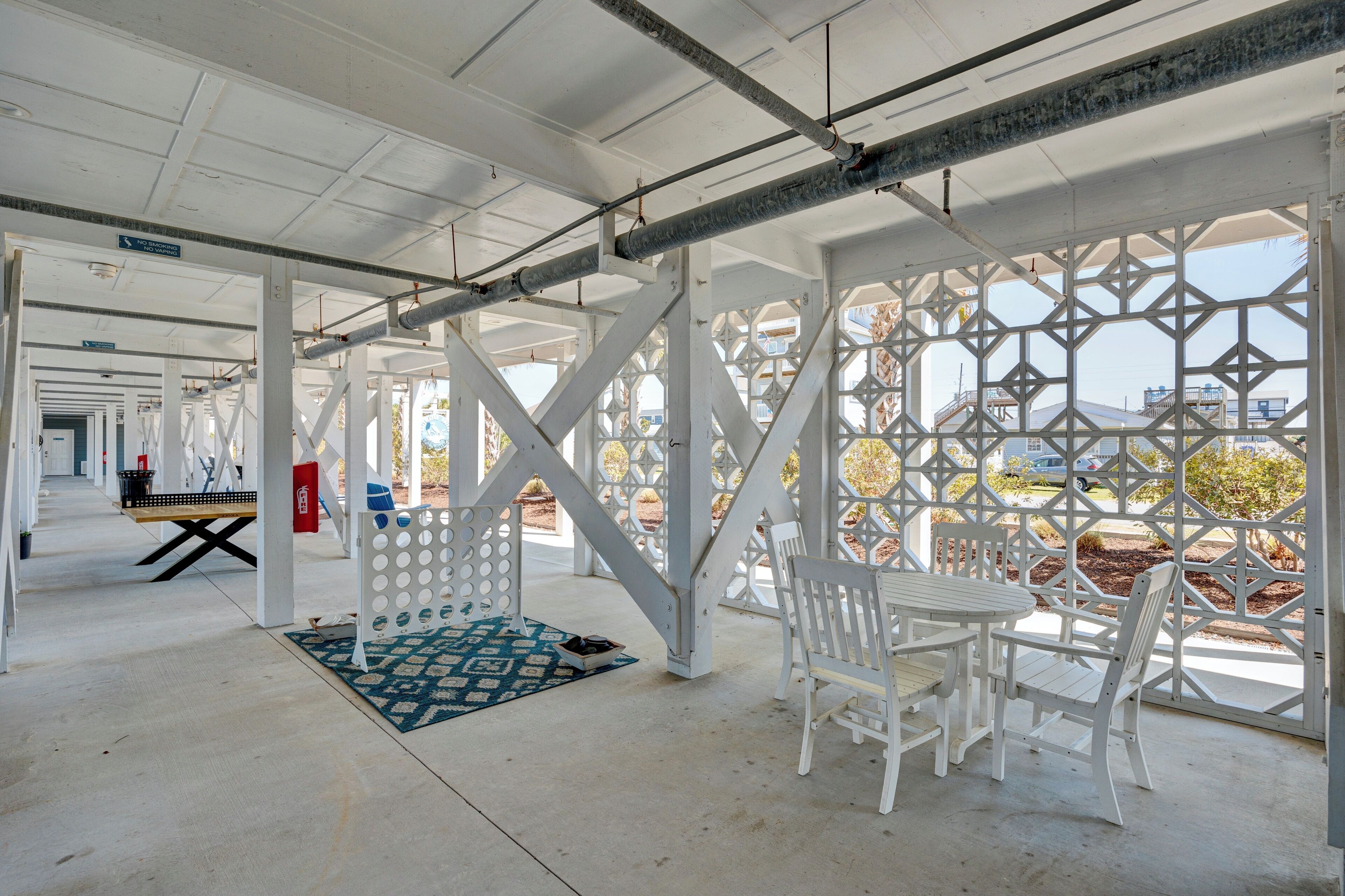 A covered outdoor area with a white table and chairs, a patterned rug, and a view of the surrounding landscape through a geometric lattice structure.