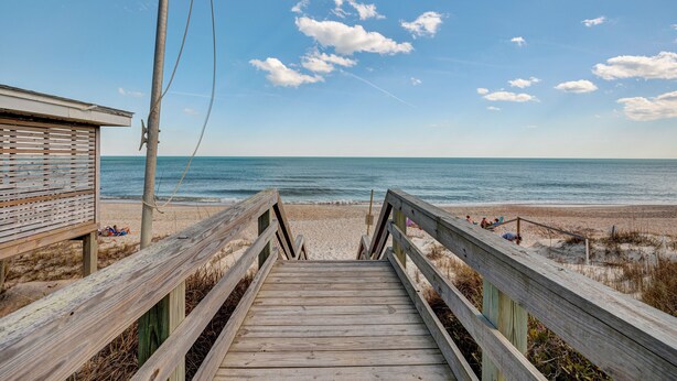 A wooden boardwalk leading to a beach with a lifeguard tower and beachgoers. - Saltwater Suites, 104 Queen Pet Friendly 1st Floor (Surf City)