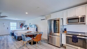 A modern kitchen with stainless steel appliances, a dining area with a round table and chairs, and a bedroom with two beds. - Saltwater Suites, 106 Queen 1st Floor (Surf City)