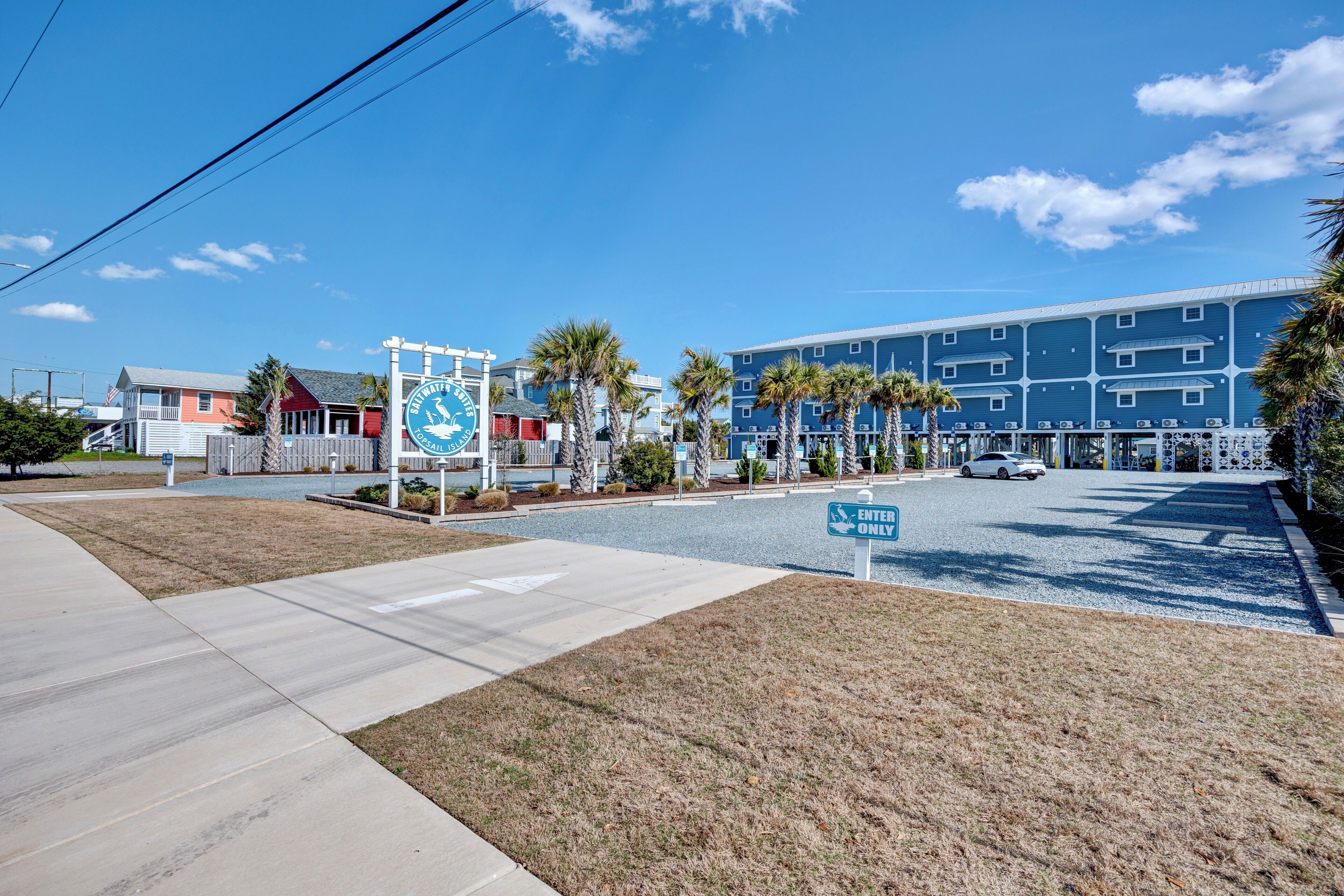 A hotel entrance with a blue building, palm trees, and a clear sky.