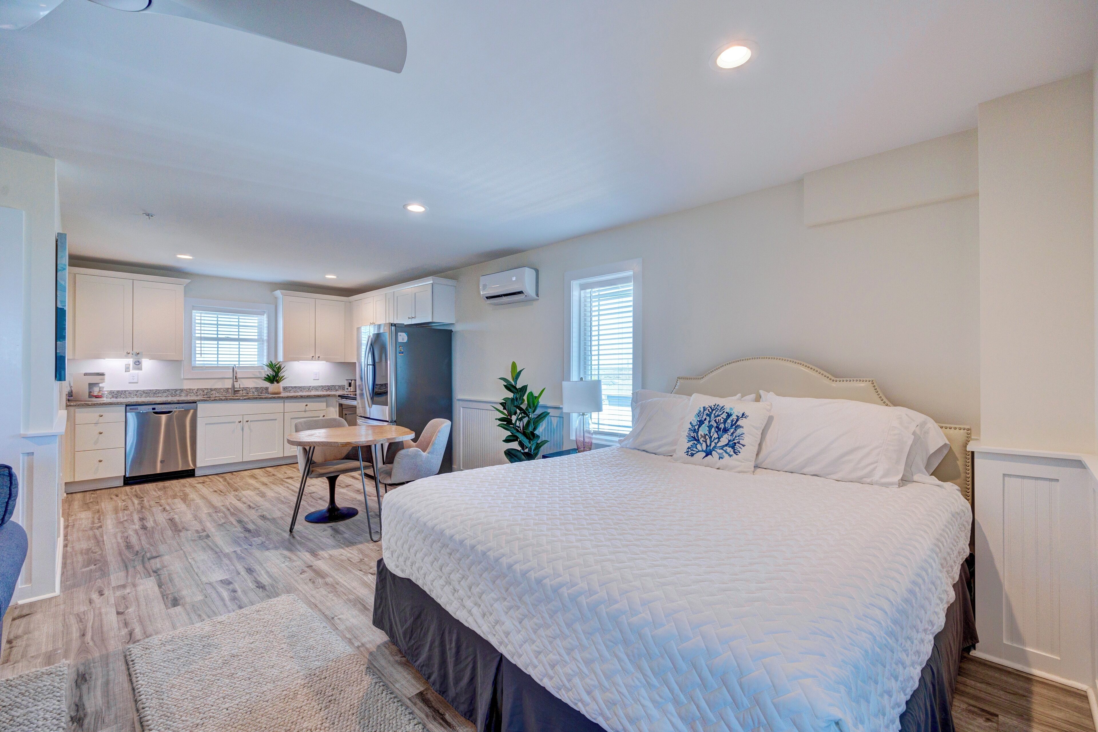 A modern hotel room with a large bed, a desk, and a kitchenette.