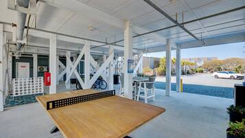 A covered outdoor seating area with a wooden table, white columns, and a view of a parking lot and buildings in the background.