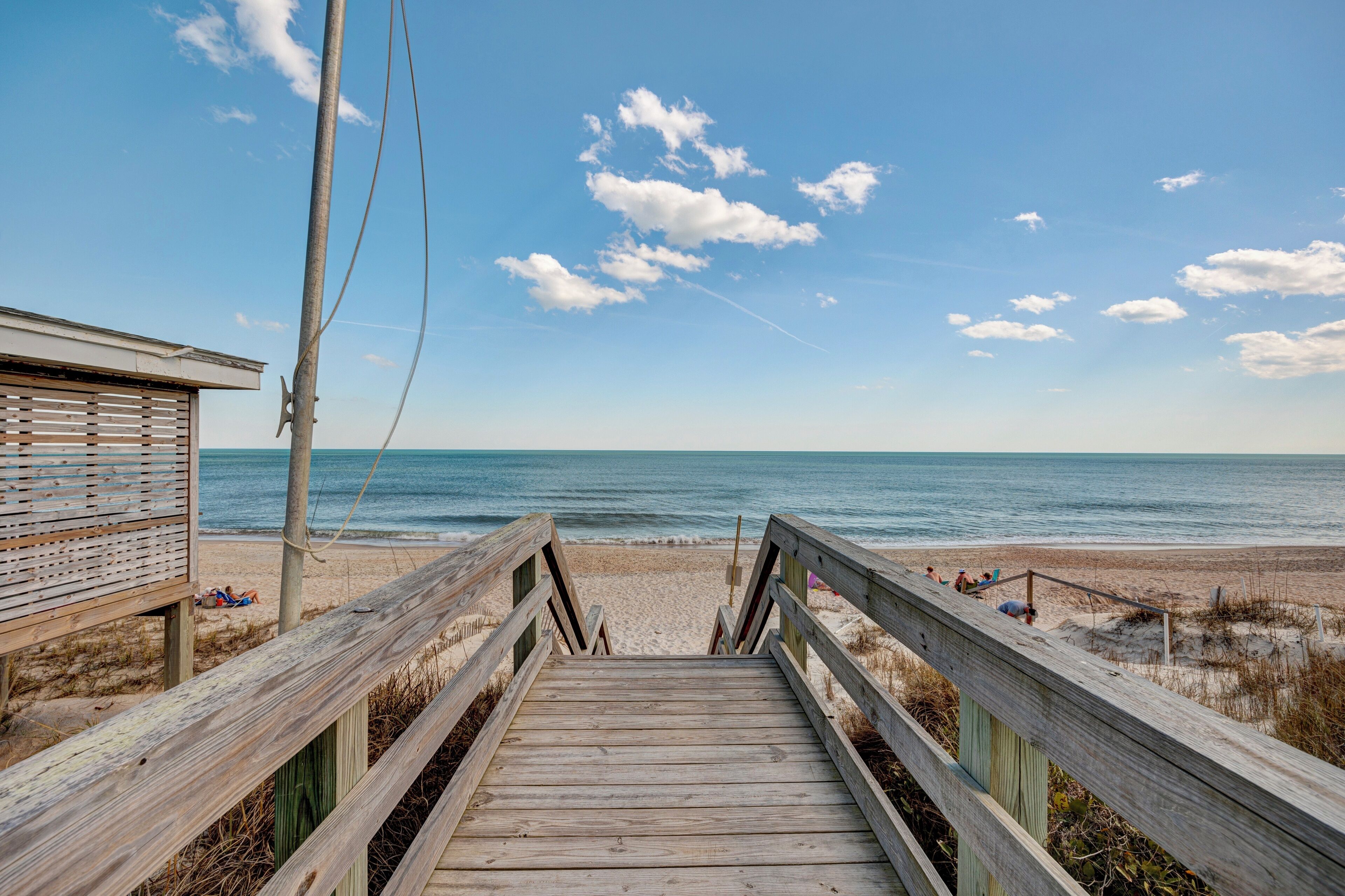 A wooden boardwalk leading to a beach with a lifeguard tower and beachgoers.