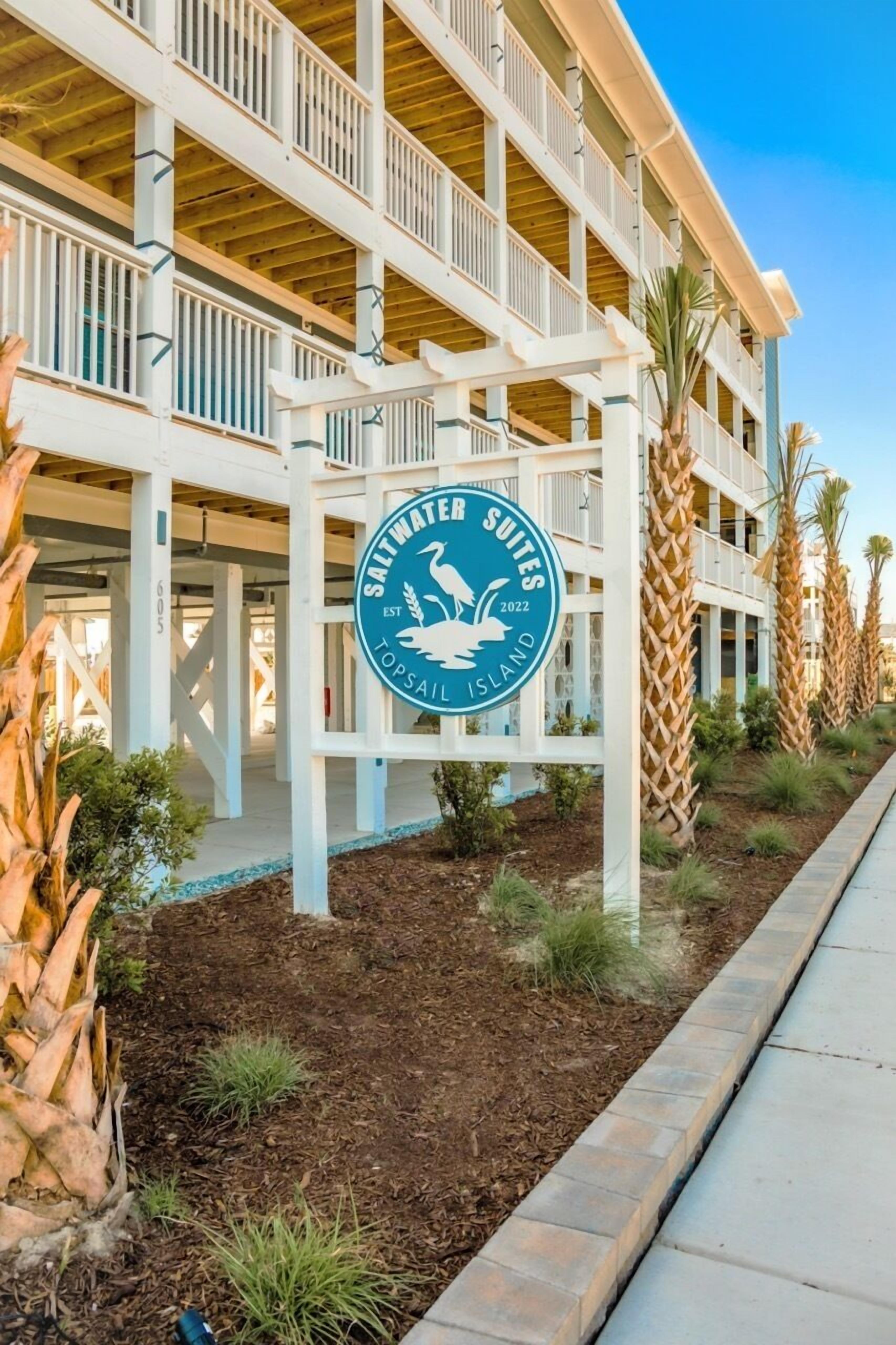 A multi-story hotel with a sign for Saltwater Suites Top Sail Island.