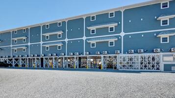 A multi-story hotel with a blue exterior, air conditioning units, and a covered outdoor area with seating.