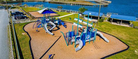 A playground with slides and swings, a picnic area, and a view of a bridge over water.