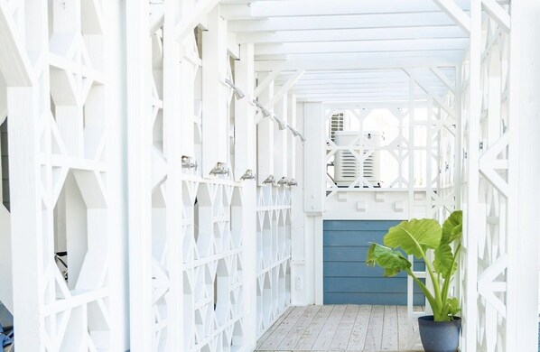 A white wooden corridor with a blue door at the end, leading to a covered area with a white ceiling and a ventilation unit.