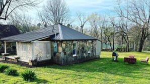 A stone building with a sloped roof, a fenced patio area, and a barbecue grill. - River Rock Cabin - Near Spring River and Main St (Mammoth Spring)