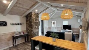 A rustic kitchen with wooden beams, a stone wall, and a wooden dining table. - River Rock Cabin - Near Spring River and Main St (Mammoth Spring)
